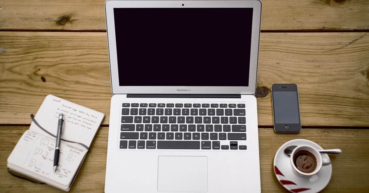 un escritorio con una computadora, una libreta, un celular y una cafe